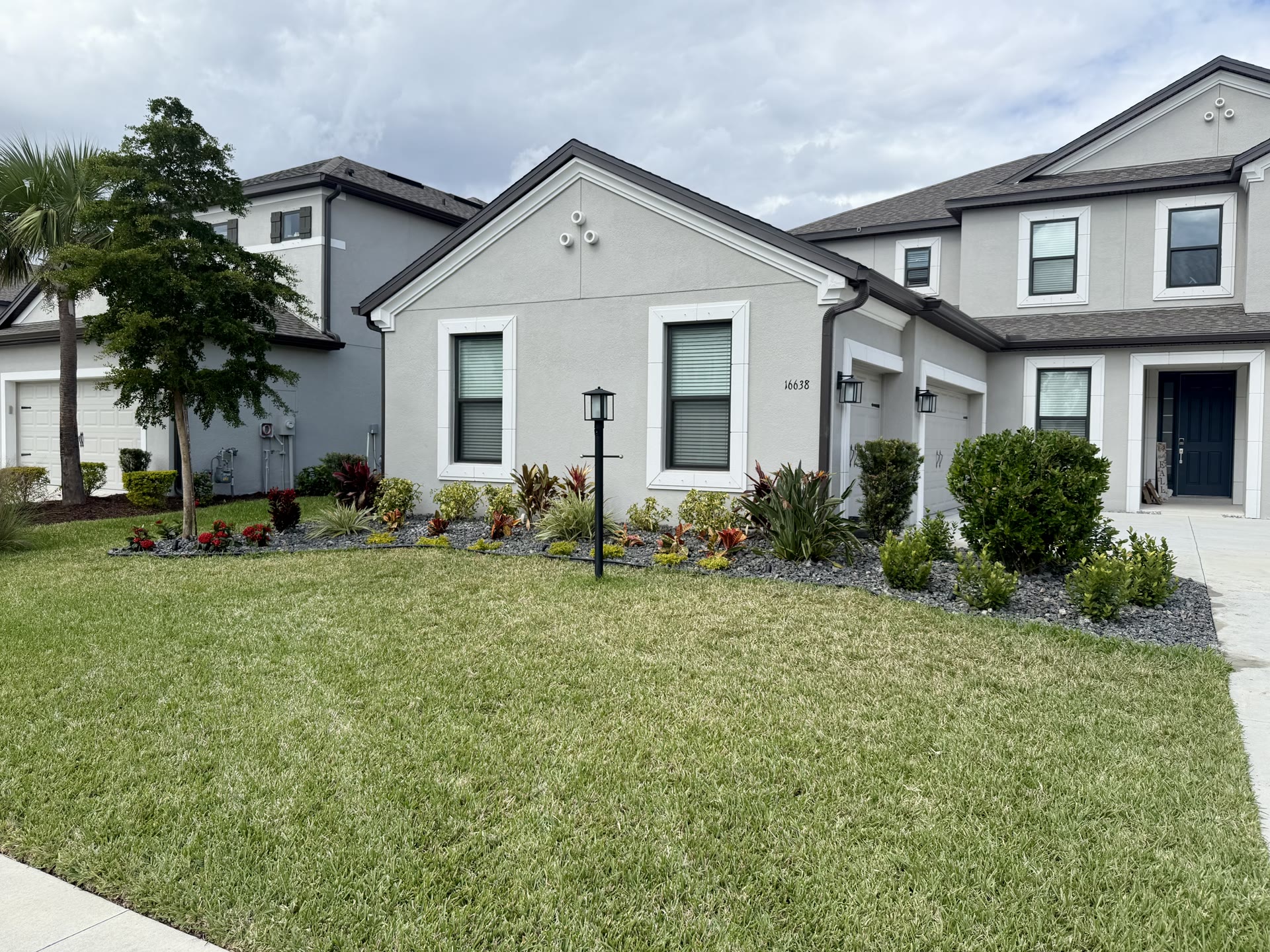 Residential front yard with manicured lawn, tropical flower beds and rock mulch