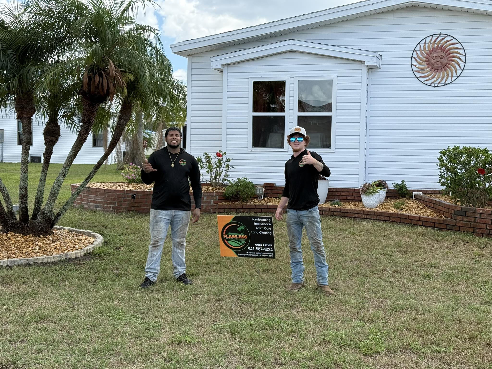 Two Flawless Palms crew members posing with company sign in front of completed landscaping job