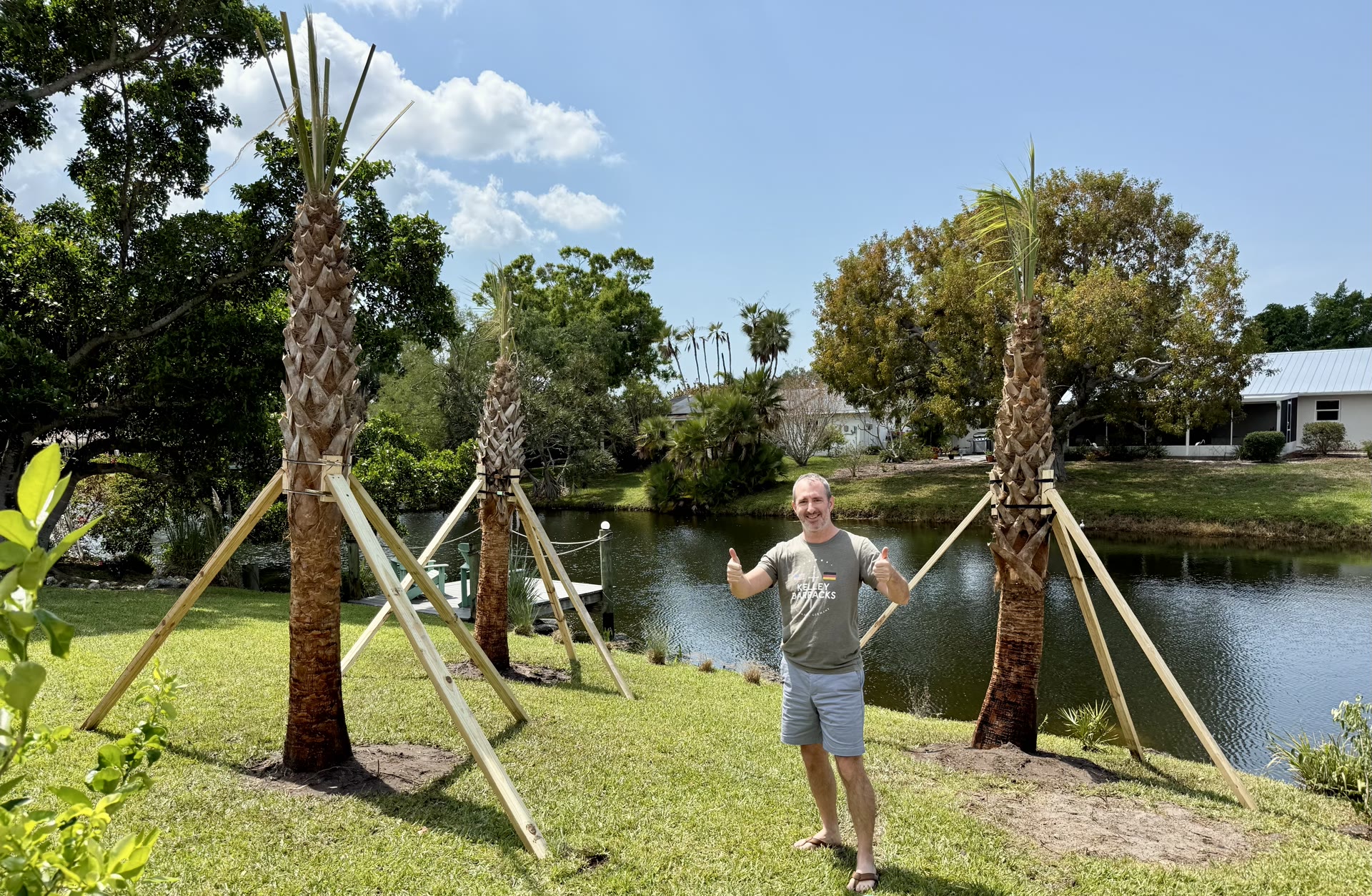 Cody Green with newly planted palms supported by stakes along a waterway